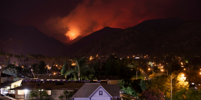 foreground image of neighborhood at night, background silhouette of hill on fire